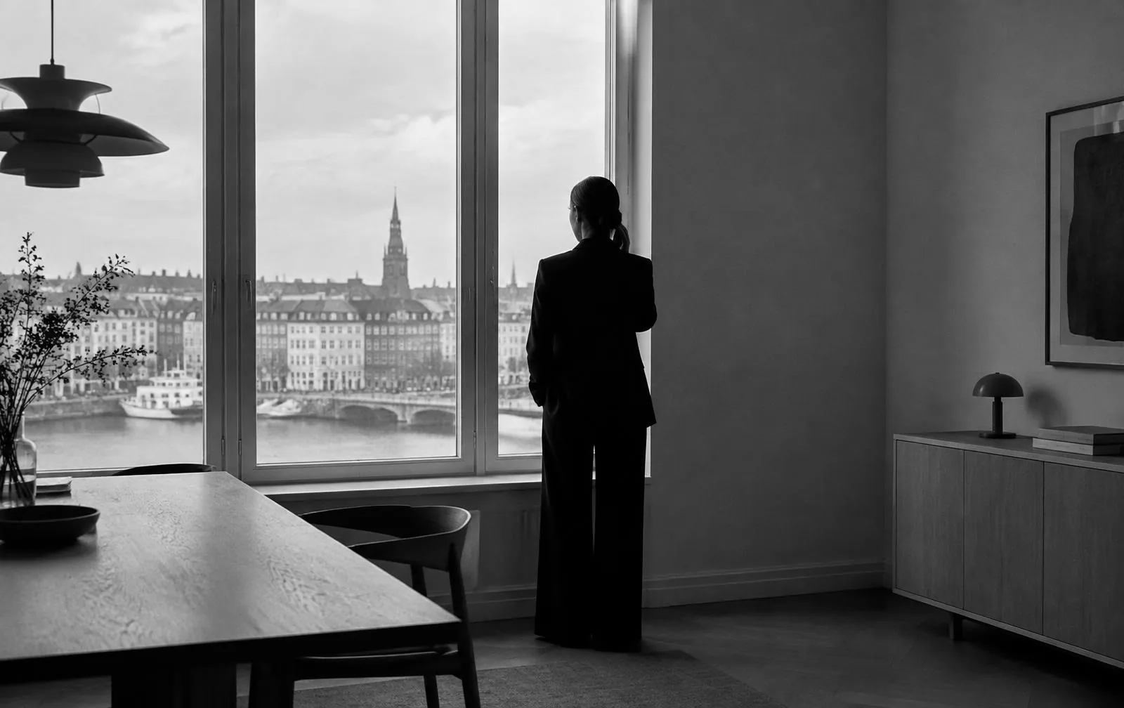 Sort-hvid silhuet af en person set bagfra ved et stort vindue over København, der taler i telefon