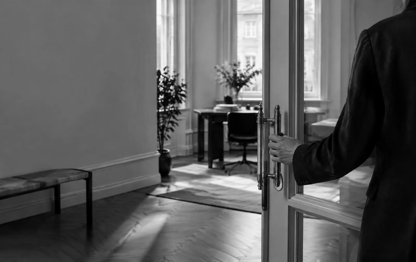 Sort-hvidt billede af en hånd, der åbner en glasdør ind til et lyst skandinavisk kontor